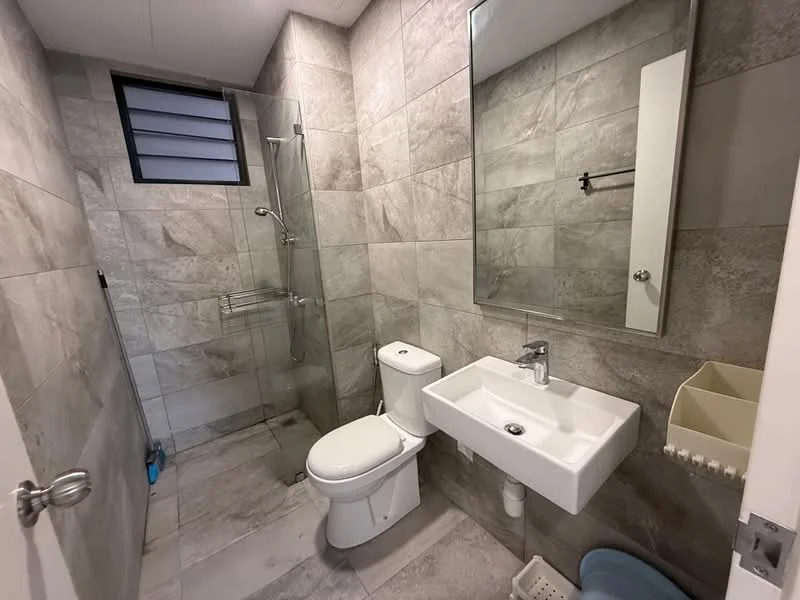 Bathroom features: grey tiled walls, grey tiled flooring, walk-in shower with glass enclosure, rain shower head, handheld shower, white toilet, white wall-mounted sink, mirror above sink, towel rack, window with horizontal slats, shower caddy, blue storage bin; style: modern.