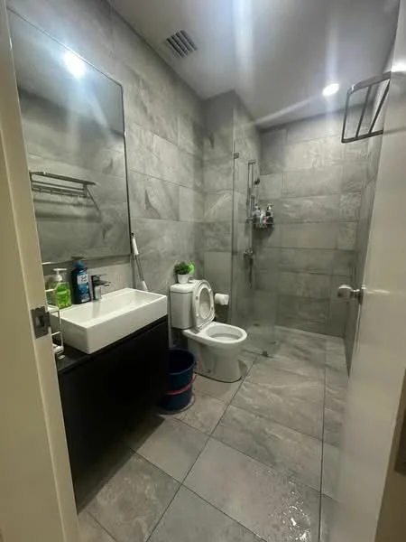 Bathroom features: grey marble tile flooring, grey tile walls, single-sink vanity with black cabinet, chrome basin mixer faucet, framed mirror, one-piece toilet, walk-in shower with glass enclosure, shower head, towel rack, shelf above sink, decorative plant; style: modern.