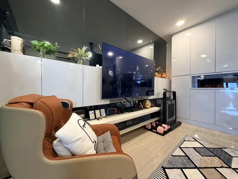 Living features: grey wall with glossy finish, white cabinetry with flat-panel design, large wall-mounted TV, light wood flooring, decorative plants on shelves, black and white area rug with geometric pattern, comfortable brown armchair, open shelving unit, built-in kitchen area with appliances, decorative items on shelves; style: modern.