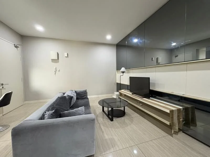 Living features: grey fabric sofa, black round coffee table, TV console with wooden finish, wall-mounted TV, large mirror on wall, recessed downlights, cream painted walls, glossy black cabinetry, tile flooring, floor-to-ceiling windows, decorative lamp; style: modern.