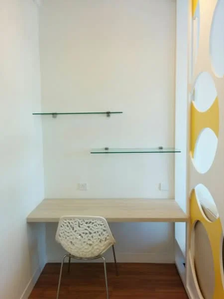 Room features: white painted walls, wooden flooring, glass shelves, light wood desk, decorative wall with circular cutouts, modern chair with intricate design; style: modern.