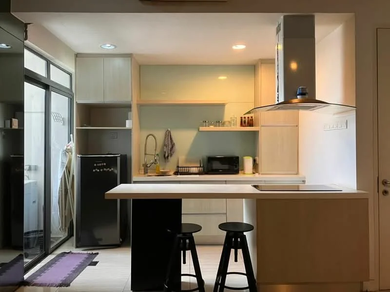 Kitchen features: white cabinetry, black countertop, single-bowl stainless-steel sink, chrome pull-down faucet, built-in microwave, black fridge, open shelving, kitchen island with seating, recessed downlights, floor-to-ceiling windows, sliding glass door, vinyl plank flooring; style: modern; view: garden.