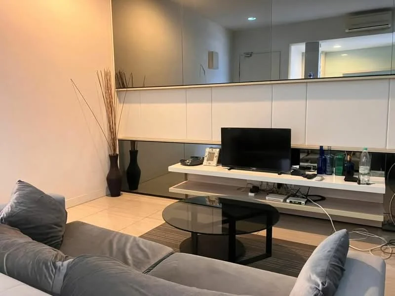 Living features: grey fabric sofa, black glass coffee table, TV console with storage, wall-mounted TV, decorative vase, decorative plant, mirrored wall, recessed lighting, cream painted walls, tile flooring, air conditioning unit; style: modern.