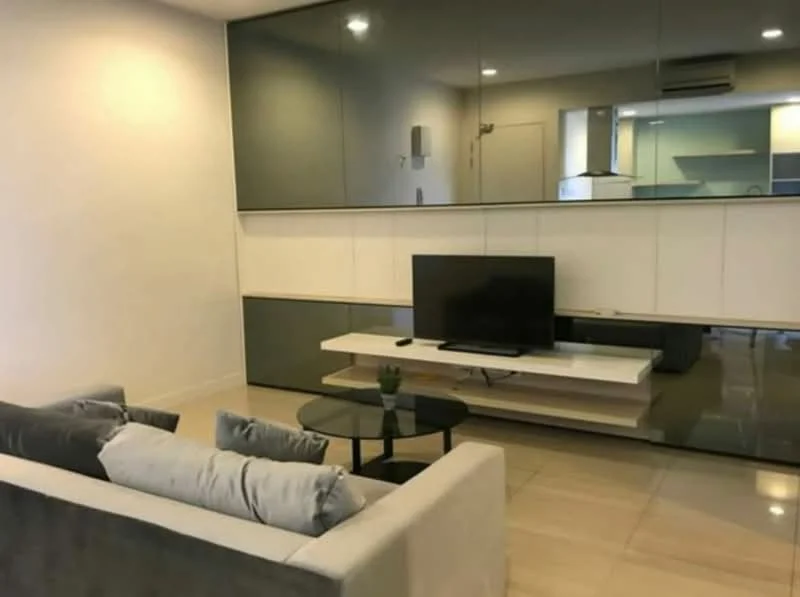 Living features: grey fabric sofa, glass coffee table, wall-mounted TV, white TV console, mirrored wall panel, recessed lighting, cream painted walls, tile flooring, wall-mounted air conditioning unit; style: modern.