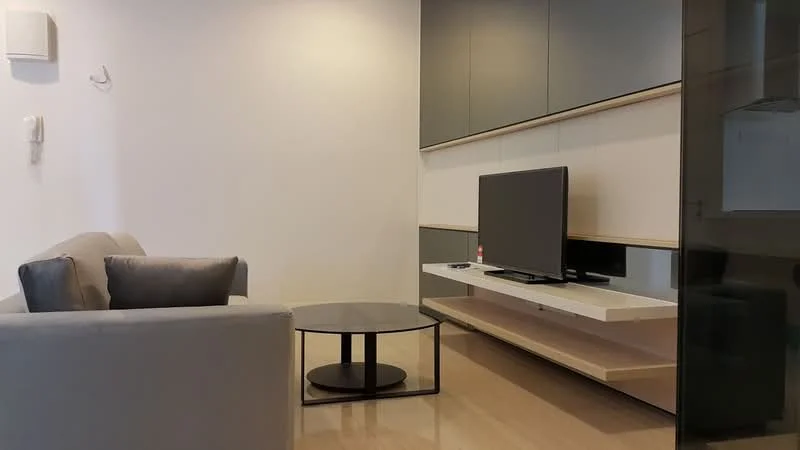 Living features: light grey fabric sofa, round glass coffee table with black base, wall-mounted TV, white TV console, dark cabinetry, cream painted walls, laminate flooring, recessed lighting, air conditioning unit on wall; style: modern.
