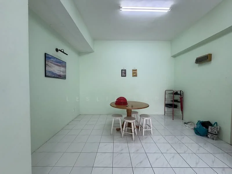 Dining features: light green painted walls, white tiled flooring, round wooden dining table, three white stools, wall-mounted air conditioning unit, framed artwork on wall, two small framed pictures on wall, open space with minimal furniture; style: minimalist.