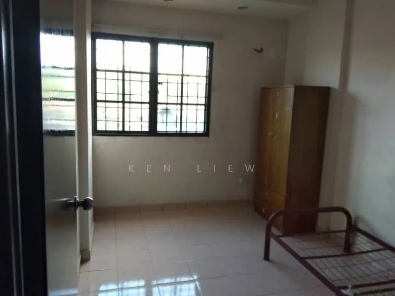 Room features: two windows with metal grills, light-colored walls, tiled flooring, wooden wardrobe, metal bed frame without mattress, single light fixture on ceiling, corner wall with no visible decor, neutral color scheme.