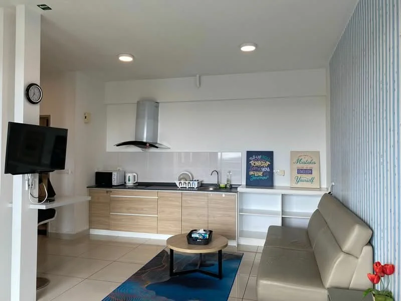 Living features: grey leather sofa, round coffee table, wall-mounted TV, pendant light, kitchenette with wooden cabinetry, white backsplash, stainless-steel range hood, built-in microwave, kettle, sink, countertop with bar seating, decorative wall art, blue accent wall, tile flooring; style: modern.