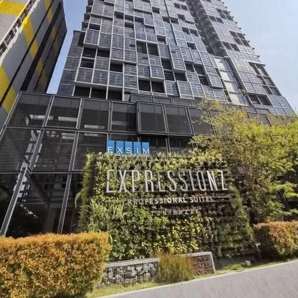 Exterior type: high-rise condominium; features: glass curtain wall, green wall with plants, prominent signage, modern facade with metal accents, surrounding landscaping with shrubs, multiple storeys, balconies on upper floors; style: modern.