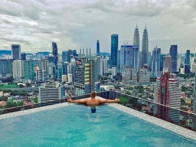Exterior type: high-rise condominium; features: infinity pool, city skyline view, surrounded by urban landscape, glass railing, pool deck with loungers, modern architectural design; style: modern.