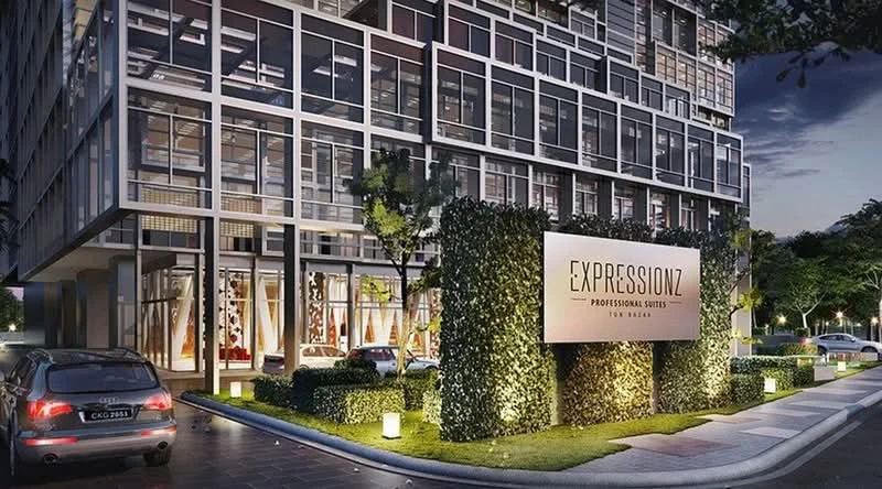 Exterior type: high-rise condominium; features: glass curtain wall facade, landscaped entrance with greenery, illuminated signage, manicured hedges, paved driveway, parking spaces, outdoor lighting, modern architectural design; style: contemporary.