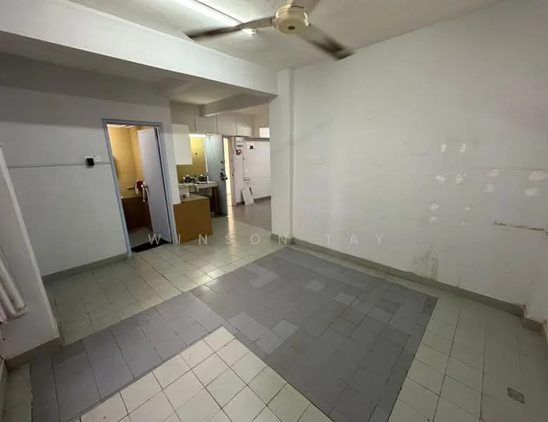 Room features: white painted walls, grey tiled flooring, ceiling fan, open layout, kitchen area visible, doorway leading to another room, light switch on wall, no visible furniture.