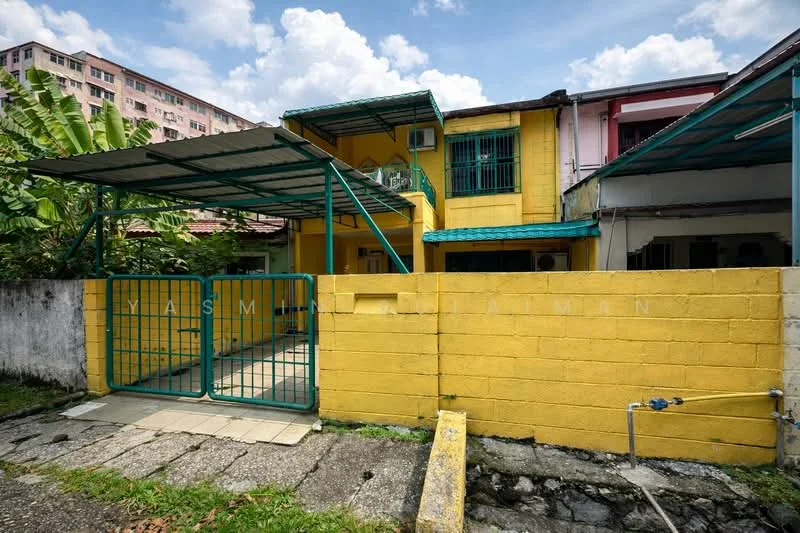 Exterior type: semi-detached house; features: yellow painted facade, metal roof, covered car porch, front gate with metal bars, exposed concrete wall, paved walkway, surrounded by greenery, air conditioning unit visible, two-storey structure, balcony on upper level; style: modern.