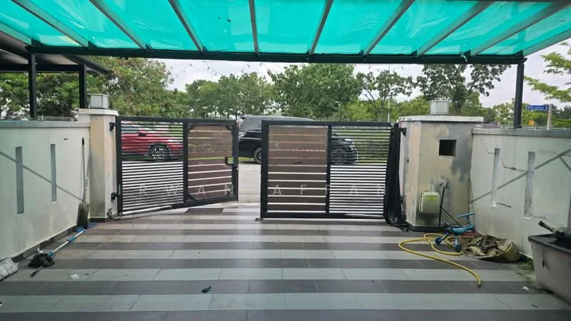 Exterior features: metal gate, sliding gate mechanism, paved flooring, green canopy roof, surrounding greenery, visible vehicles in background, concrete walls, water hose on ground; style: modern.
