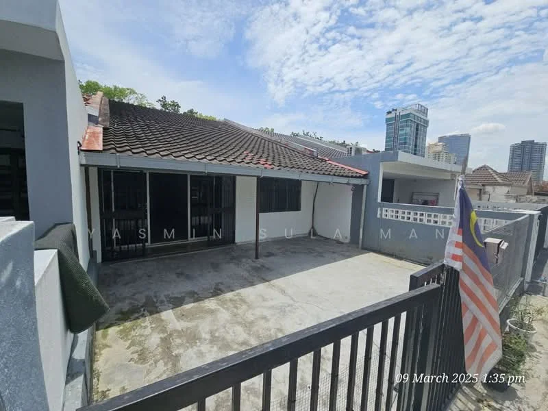 Exterior type: detached bungalow; features: flat roof, grey painted facade, concrete flooring, fenced perimeter, flagpole with Malaysian flag, surrounded by urban landscape, visible city skyline in background; style: modern.