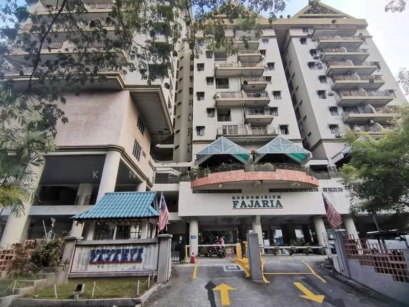 Exterior type: mid-rise condominium; features: cream painted facade, glass awning at entrance, multiple storeys, balconies on upper floors, landscaped entrance area, security gate at entrance, parking area visible, flag poles with flags, surrounded by greenery; style: modern.