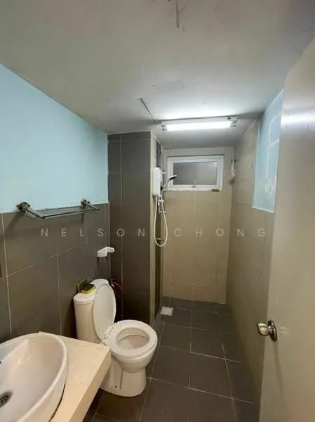 Bathroom features: white toilet, single-sink vanity with countertop, shower with wall-mounted shower head, tile flooring, grey wall tiles, light blue painted walls, mirror above sink, window for natural light, overhead fluorescent lighting.