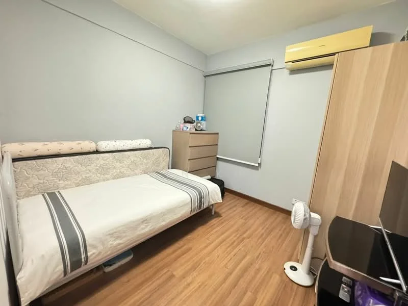 Bedroom features: single bed with mattress, light grey painted walls, wooden flooring, built-in wardrobe, window with roller blinds, wall-mounted air conditioning unit, desk with chair, table lamp, fan on floor; style: modern.
