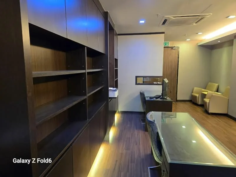 Room features: wooden flooring, built-in wooden shelving, glass-top desk, wall-mounted air conditioning unit, recessed lighting, neutral wall color, seating area with two armchairs, TV console; style: modern.