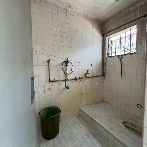 Bathroom features: white tiled walls, white tiled flooring, shower area with step-up, exposed plumbing, window for natural light, green plastic bucket, metal showerhead, wall-mounted faucet, metal hooks on wall.
