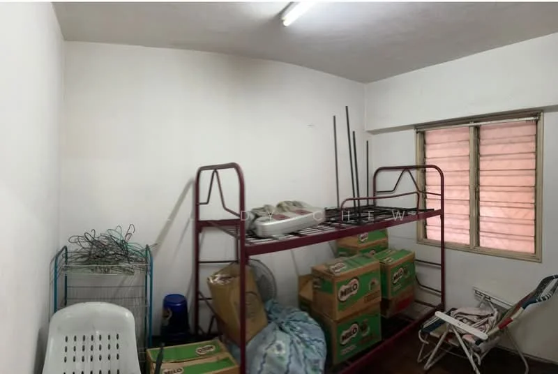 Room features: white painted walls, wood flooring, single window with wooden frame, metal shelving unit, plastic chair, stacked cardboard boxes, fan, various wires and cables.