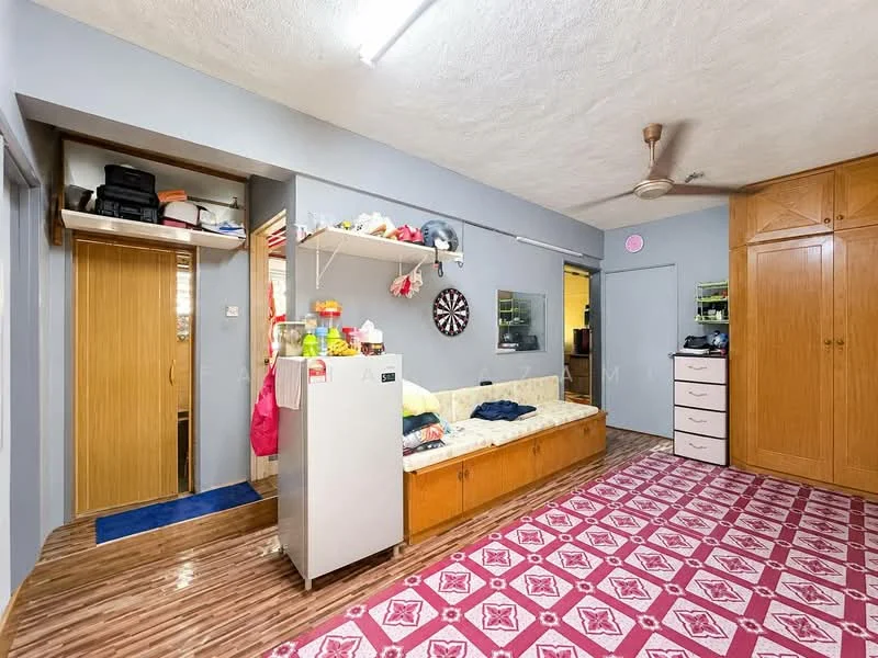 Living features: laminate flooring, grey painted walls, ceiling fan, sofa with cushions, refrigerator, wooden cabinetry, built-in wardrobe, decorative wall shelf, dartboard on wall, area rug with geometric pattern, door leading to another room.