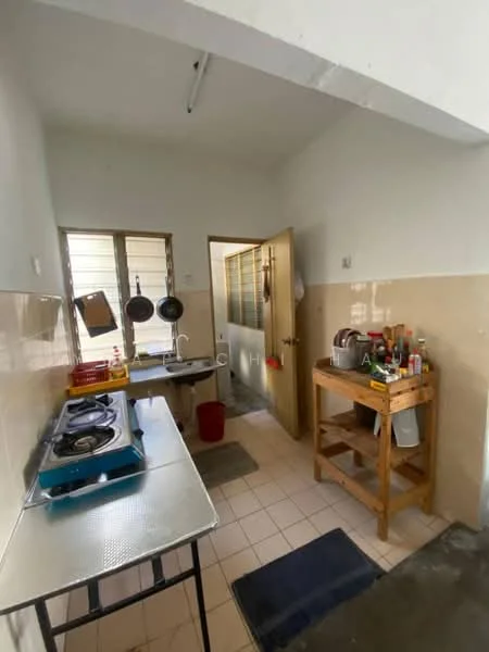 Kitchen features: white painted walls, cream tiled backsplash, tile flooring, stainless-steel gas stove, wooden kitchen cart, hanging pots, window with metal grille, door leading to another room, sink, kitchen utensils on countertop, red bucket.