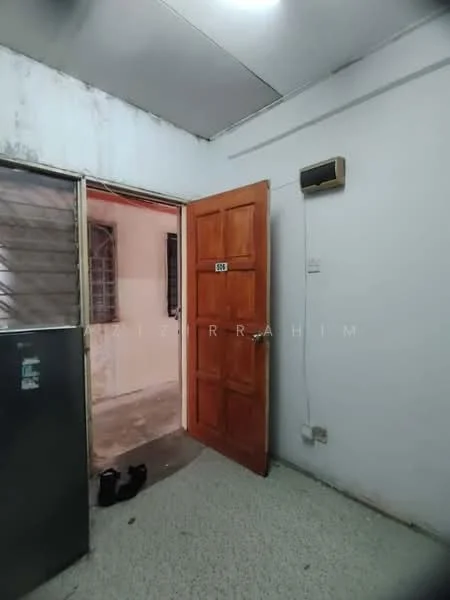 Room features: wooden door, white painted walls, exposed concrete flooring, window with metal grille, wall-mounted air conditioning unit, visible electrical outlet, door frame, shoes on the floor.