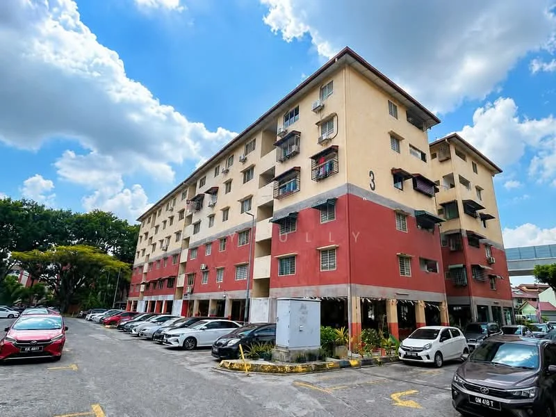 Exterior type: low-rise apartment block; features: 5-storey building, red and cream painted facade, balconies with metal railings, ground-level parking area, landscaped garden area, multiple car parking spaces, surrounded by greenery, clear blue sky, clouds in the background; style: traditional.