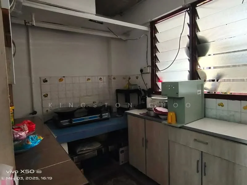 Kitchen features: white tiled walls, grey laminate cabinetry, blue countertop, single-bowl stainless-steel sink, chrome pull-down faucet, freestanding gas stove, exhaust hood, window with horizontal slats, tile flooring, open shelving, kitchen utensils on countertop, food items in bowls.