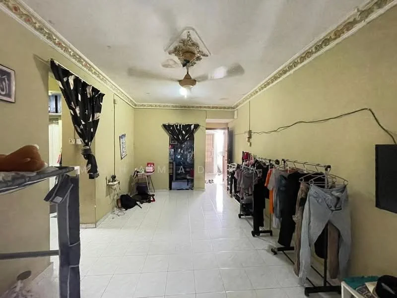 Room features: white painted walls, white tiled flooring, ceiling fan, decorative ceiling rose, doorway leading outside, hanging clothes rack, clothes on hangers, window with black curtains, light fixture on ceiling, wall-mounted TV, floor space with minimal furniture.