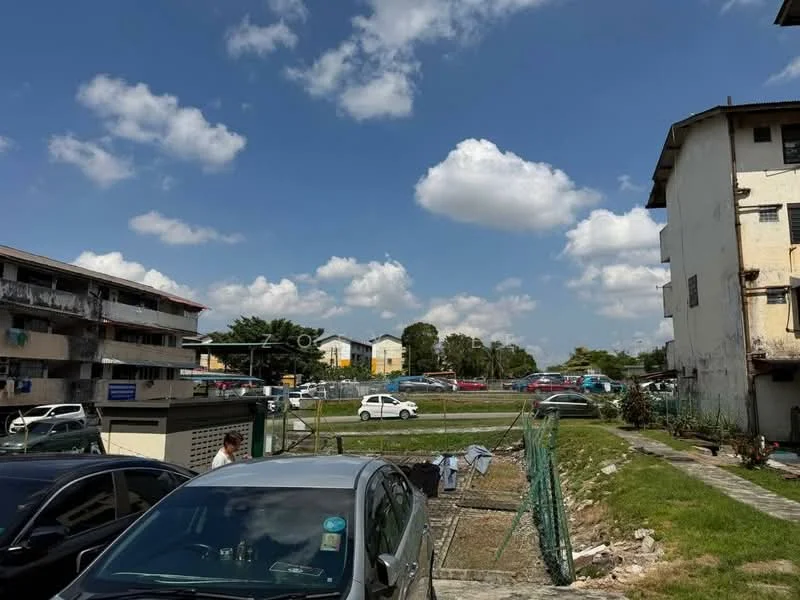 Exterior type: low-rise apartment block; features: two-storey low-rise buildings, concrete facade, visible parking area, manicured lawn, surrounding greenery, open space in front of buildings, fenced area, cloudy sky, multiple parked cars; style: modern.