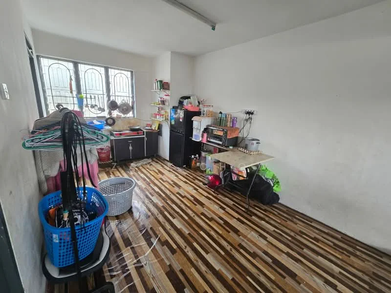 Room features: wooden flooring, white painted walls, two large windows with metal grilles, black cabinet, table with various items, blue laundry basket, white laundry basket, clothes drying rack, shelves with storage containers, wall-mounted electrical outlets.