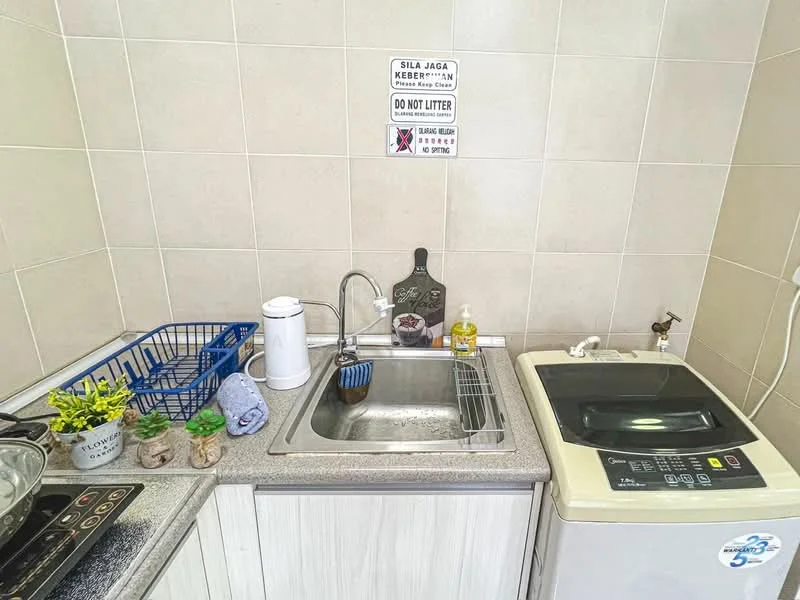 Kitchen features: single-bowl stainless-steel sink, chrome pull-down faucet, grey laminate countertop, white cabinetry, built-in washing machine, ceramic tile backsplash, kitchen towel, small potted plants, dish soap, sign on wall; style: modern.