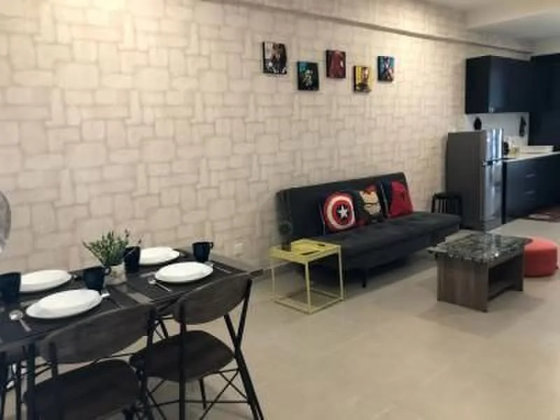 Living features: grey fabric sofa, coffee table with glass top, black dining table with 4 chairs, decorative wall art, light-colored stone accent wall, refrigerator, kitchen cabinetry, countertop, floor tiles, small red ottoman; style: modern.