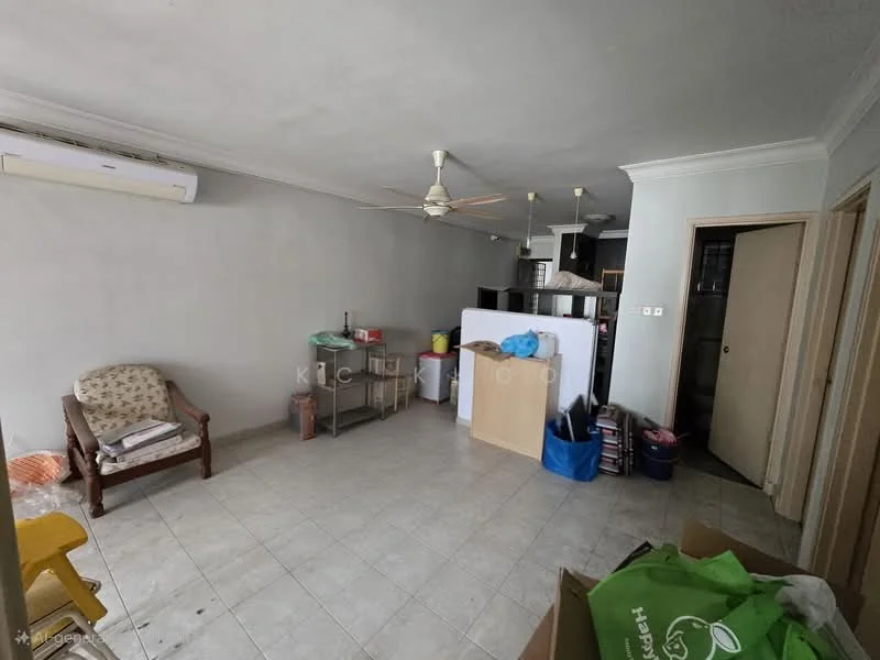 Living features: tiled flooring, white painted walls, ceiling fan, wall-mounted split AC, wooden door, open layout to kitchen, furniture including armchair, metal shelving unit, boxes and bags on the floor. Kitchen features: kitchen counter, open layout, visible appliances, storage cabinets.