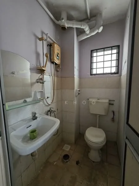 Bathroom features: white ceramic toilet, single-sink vanity with wall-mounted faucet, mirror above sink, shower head with wall-mounted holder, exposed plumbing, grey tiled walls, cream tiled flooring, small window for ventilation.