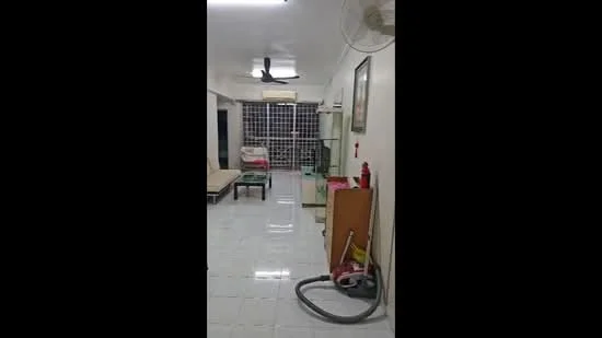 Room features: white painted walls, glossy white tile flooring, 5-blade ceiling fan, wall-mounted air conditioning unit, large window with security grille, sofa, coffee table, glass display cabinet, vacuum cleaner, fire extinguisher, decorative wall art; style: modern.