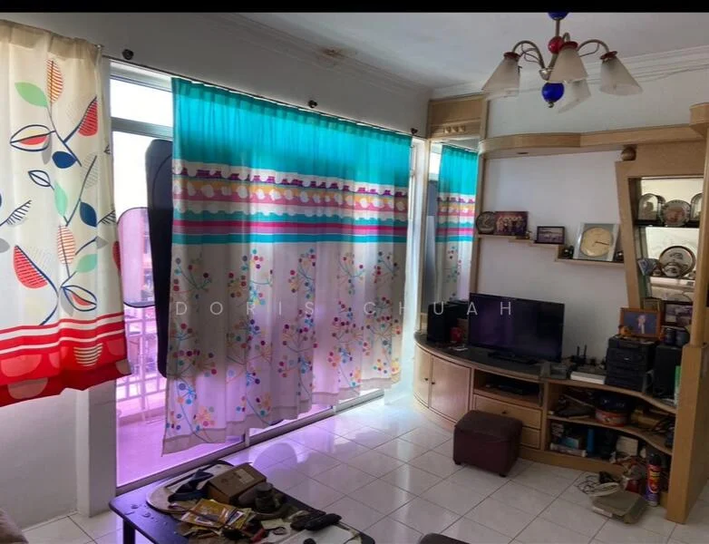 Living features: white tiled flooring, light blue curtains with floral pattern, cream walls, wooden entertainment unit, wall-mounted TV, decorative wall shelves, ceiling light fixture with multiple bulbs, various decorative items on shelves, small brown storage box, open balcony door, window with sheer curtains; style: contemporary; view: city.