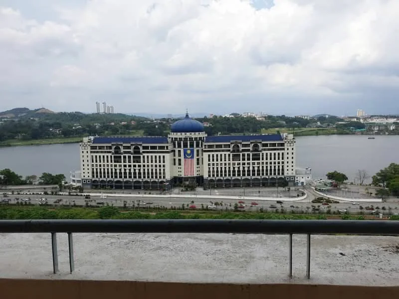 Exterior features: waterfront view, multi-storey building, blue dome, large windows, balconies, landscaped grounds, surrounding greenery, urban skyline in background; style: modern.