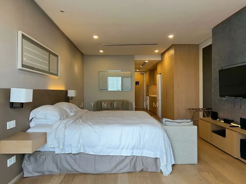 Bedroom features: king-size bed with white bedding, upholstered headboard, wooden bedside tables, wall-mounted TV, light wood flooring, recessed ceiling lights, large window with city view, built-in wardrobe, sofa at foot of bed, decorative wall paneling, neutral wall color; style: modern; view: city. Kitchen features: open kitchen layout, white cabinetry, stainless-steel appliances, built-in refrigerator, microwave, countertop with bar seating, light wood cabinetry, tile backsplash; style: modern.