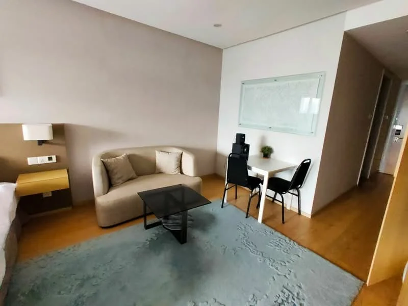 Living features: light wood flooring, beige fabric sofa, black coffee table, small dining table with two black chairs, wall-mounted artwork, wall sconce, floor-to-ceiling window, neutral painted walls; style: modern.
