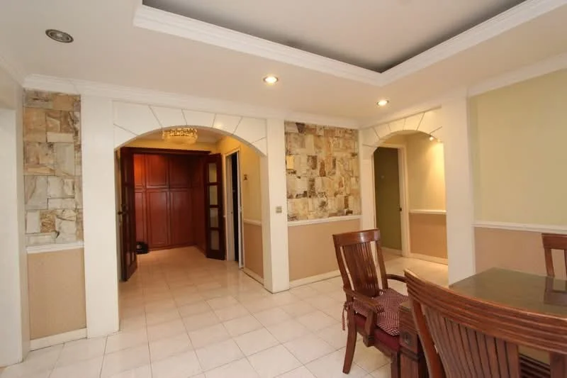 Room features: white painted walls, stone accent wall, tile flooring, crown moulding, recessed lighting, archway entrances, dining table with wooden chairs, wooden cabinetry in background, neutral color scheme; style: contemporary.