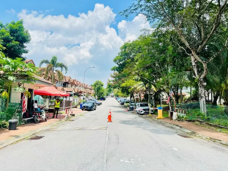Exterior type: linked terrace house; features: tree-lined street, manicured lawns, paved walkway, multiple parked cars, street vendor stall with red canopy, palm trees, greenery along the roadside, residential houses with tiled roofs, clear blue sky with clouds; style: modern.