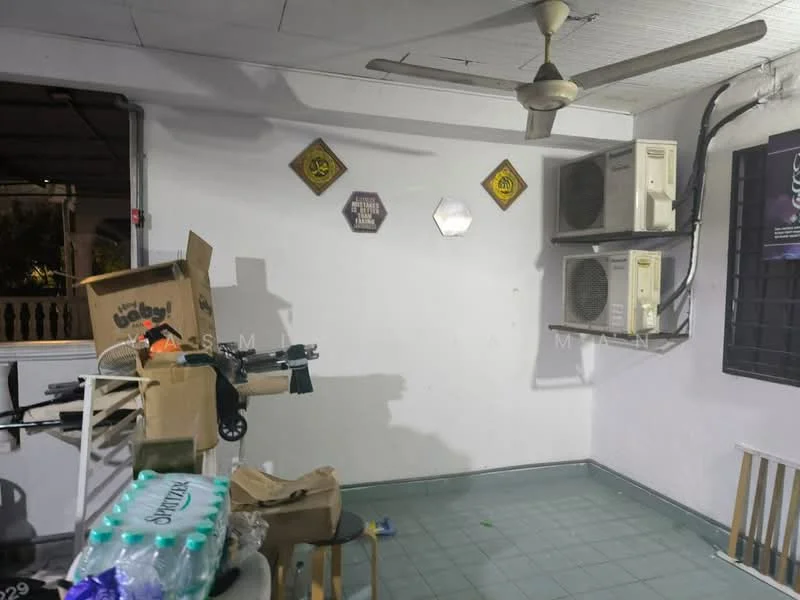 Room features: white painted walls, ceiling fan, 2 wall-mounted split AC units, green tile flooring, decorative wall plaques, stool, cardboard boxes, bottled water, window with security bars.