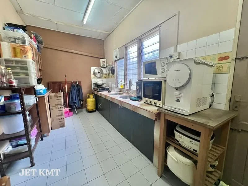 Kitchen features: grey tiled flooring, white tiled walls, wooden countertop, built-in cabinets, microwave, freestanding washing machine, kettle, toaster, 2-door refrigerator, fan, sink, storage shelves, cleaning supplies, yellow cleaning cart.