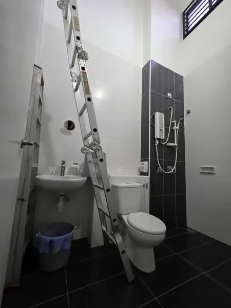Bathroom features: white painted walls, black tiled accent wall, black floor tiles, single-sink vanity with white cabinet, chrome basin mixer faucet, one-piece toilet, handheld shower, wall-mounted shower head, shower with glass partition, ladder leaning against the wall, waste bin, window for natural light; style: modern.
