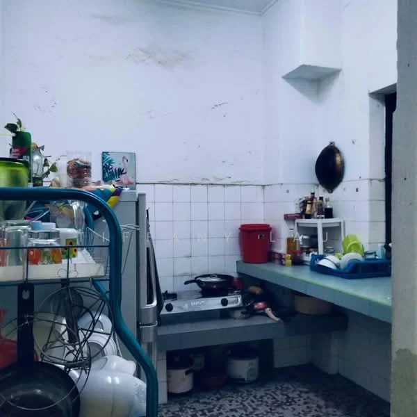 Kitchen features: white tiled walls, green countertop, stainless-steel gas stove, metal frying pan on stove, open shelving, plastic storage containers, red plastic bin, various kitchen utensils, sink with faucet, flooring with patterned tiles.