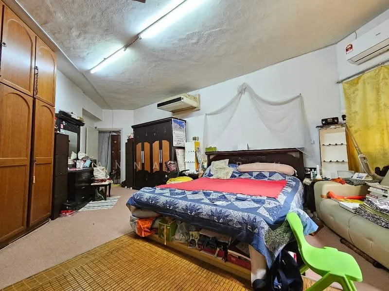Bedroom features: king-size bed with blue and red bedding, wooden headboard, built-in wooden wardrobe, dressing table with mirror, cream wall with decorative drapery, carpet flooring, air conditioning unit, green plastic chair, books and magazines on the floor, wall-mounted light fixture, sliding door to another room.