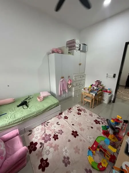 Bedroom features: single bed with green bedding, white wardrobe with drawers, pink upholstered chair, wooden table with chairs, area rug with floral pattern, toys on the floor, white painted walls, tile flooring, ceiling fan.